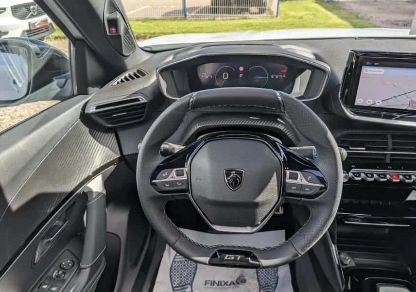 Vue intérieure centrée sur le volant GT noir avec surpiqûres vertes et tableau de bord numérique du Peugeot 2008 blanc hybride.