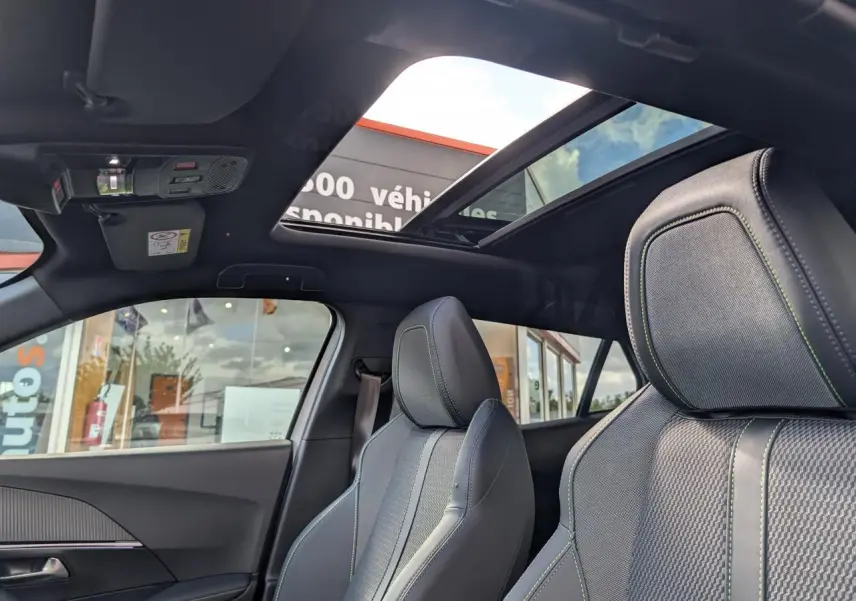 Vue intérieure avant du Peugeot 2008 GT 2026 avec toit ouvrant panoramique et sièges tissu gris à surpiqûres vertes.