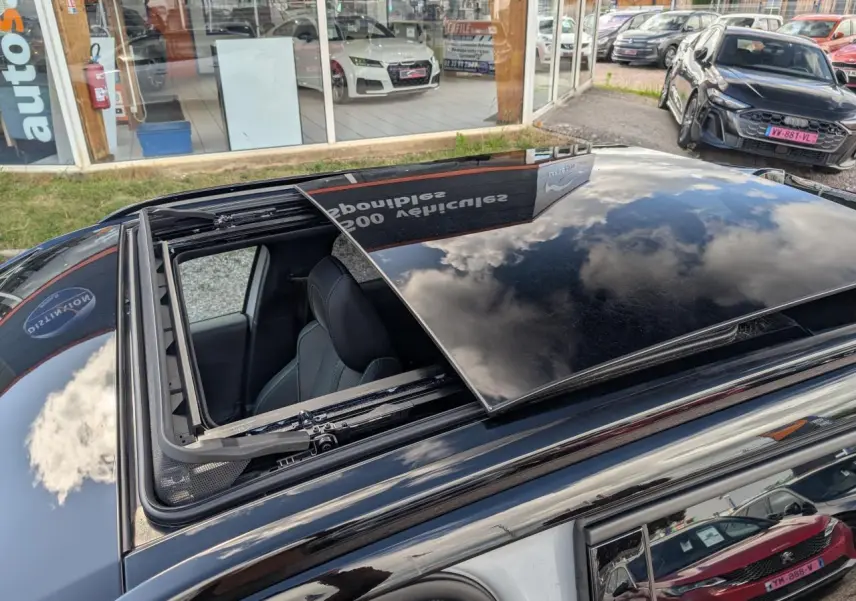 Vue en plongée sur le toit ouvrant noir ouvert d'une Peugeot 2008 blanche, avec intérieur visible côté gauche.