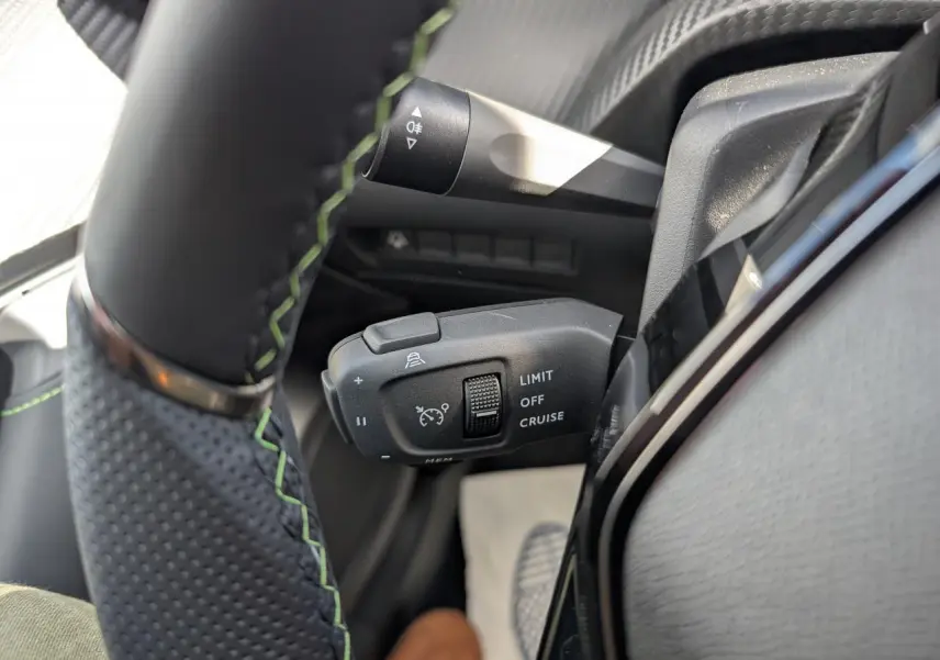 Gros plan sur la commande de régulateur de vitesse au volant cuir noir avec surpiqûres vertes du Peugeot 2008 blanc.
