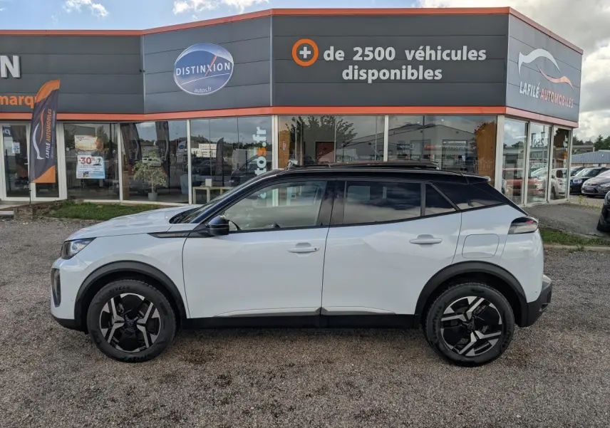 Profil droit d’un Peugeot 2008 blanc avec toit noir et jantes alliage 17'' bi-ton, stationné devant un concessionnaire.