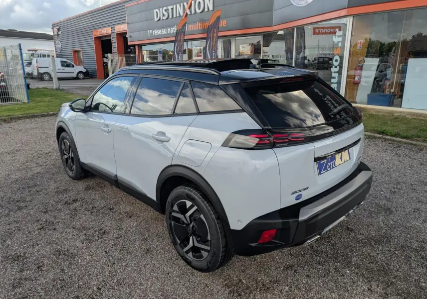 Vue 3/4 arrière droite d’un Peugeot 2008 blanc avec toit noir et jantes alliage bi-ton, stationné devant un magasin.