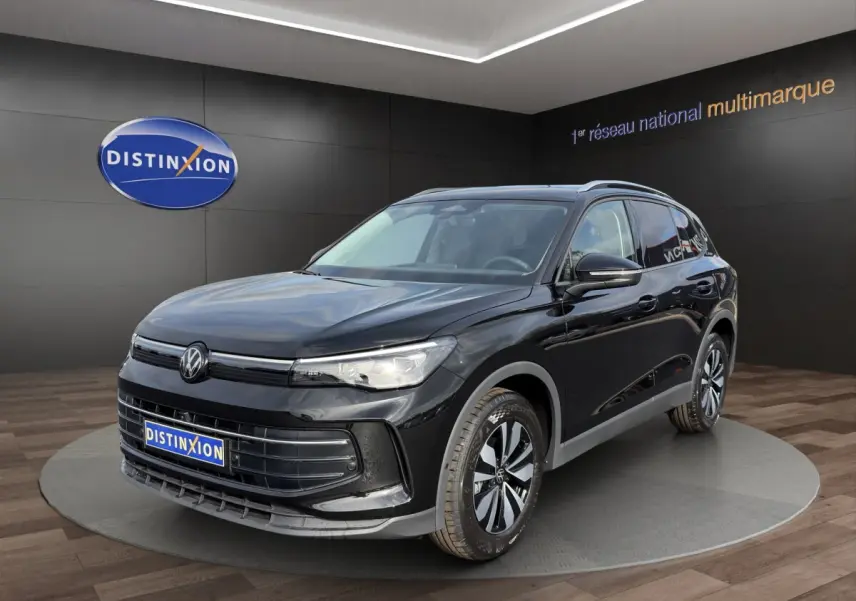 Volkswagen Tiguan noir en 3/4 avant droit, avec jantes bicolores et calandre épurée dans un showroom.