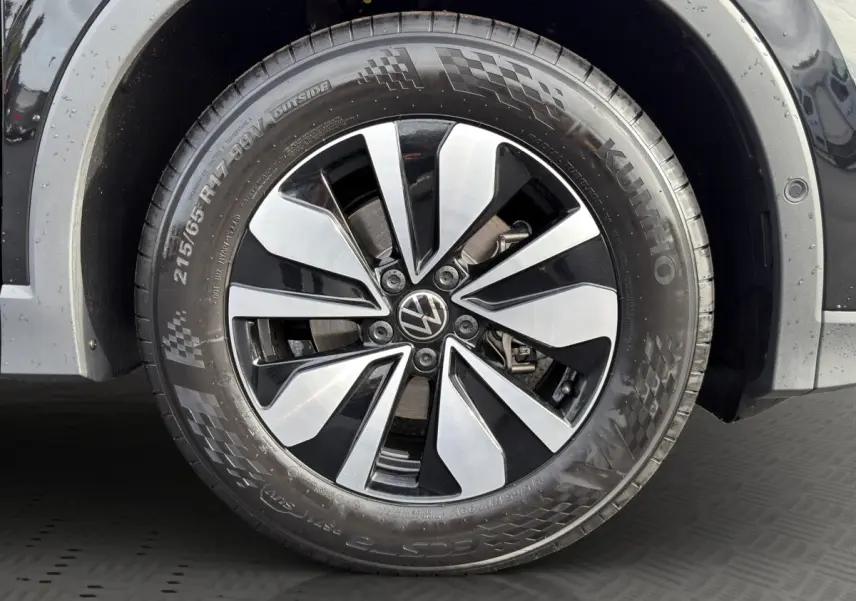 Gros plan sur la roue avant droite noire du Volkswagen Tiguan avec jante alliage bicolore et logo VW central.