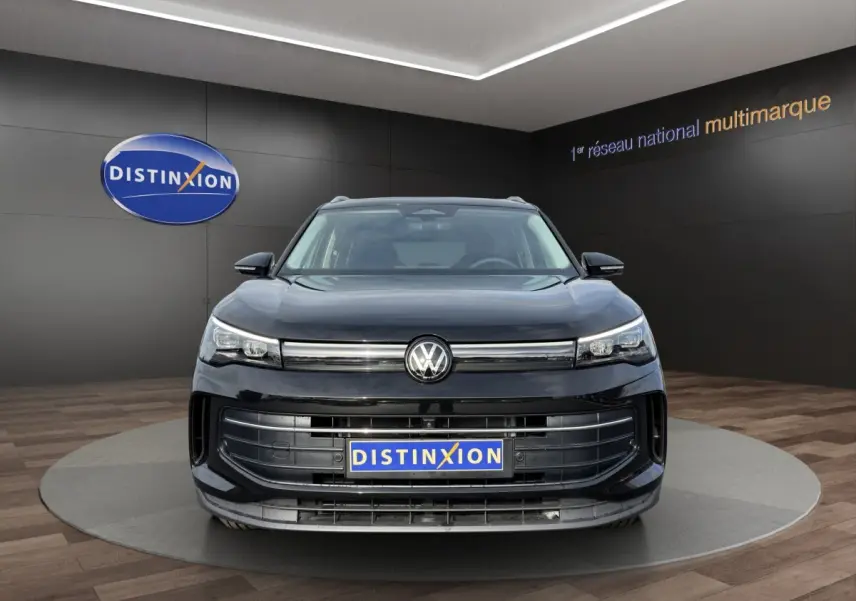 Vue frontale d'un Volkswagen Tiguan noir avec calandre large et logo VW centré, en showroom Distinxion.