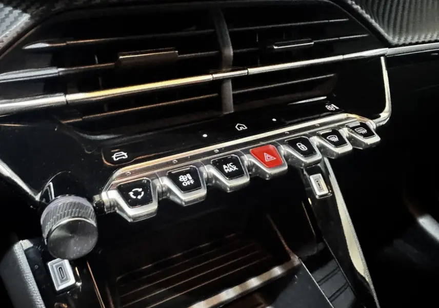 Gros plan sur la console centrale noire du Peugeot 208 2024 avec boutons de commande et port USB visible.