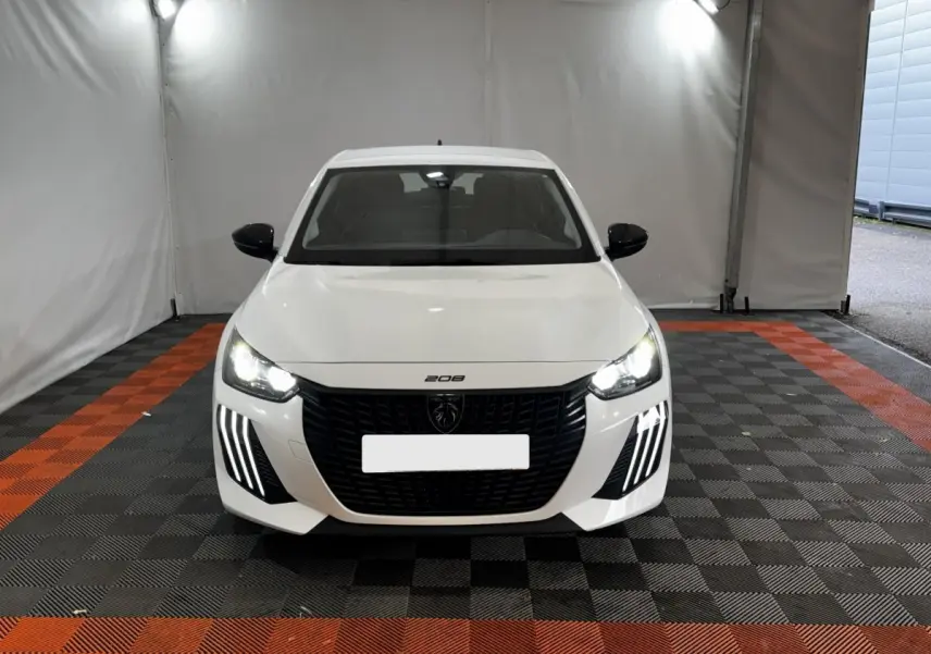 Vue de face d'une Peugeot 208 blanche 2024 avec phares LED allumés et calandre noire distinctive.