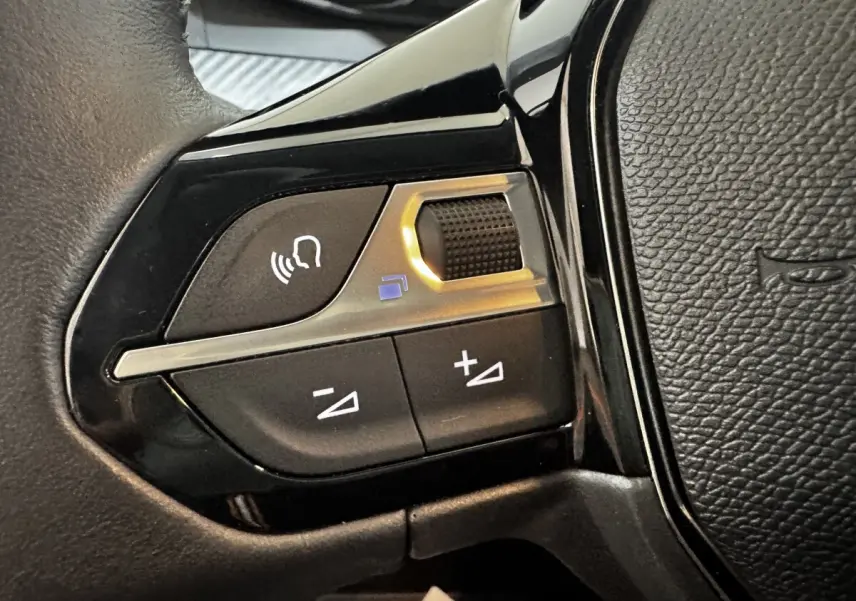 Gros plan sur les commandes vocales et volume au volant cuir noir de la Peugeot 208 PureTech 75 S&S Active.