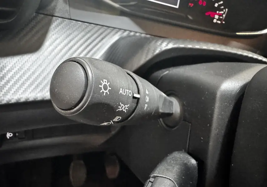 Gros plan sur la commande des phares à gauche du volant dans l’habitacle d’une Peugeot 208 blanche 2024.