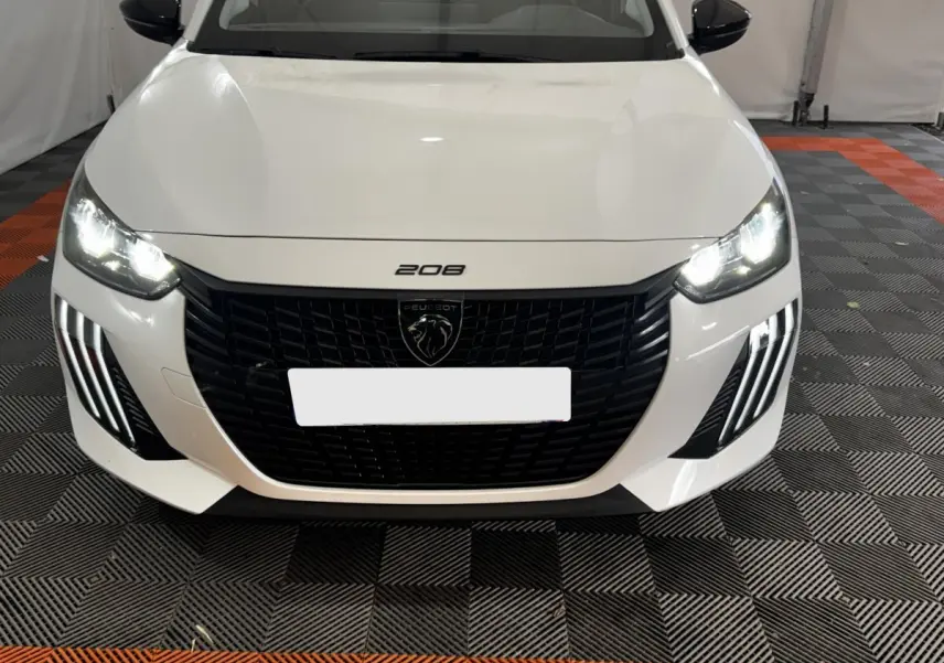 Vue avant d'une Peugeot 208 PureTech 75 S&S Active blanche avec phares LED allumés et calandre noire distinctive.