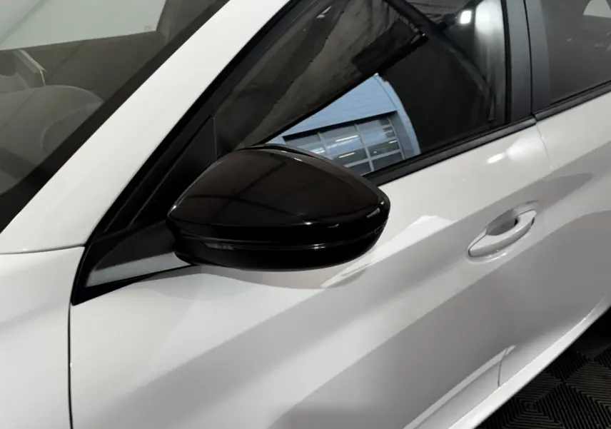 Gros plan sur le rétroviseur noir et la porte côté gauche d'une Peugeot 208 blanche vue de profil.