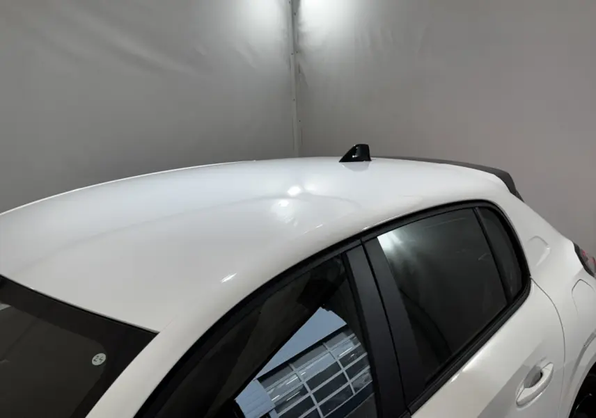 Vue 3/4 arrière droite d'une Peugeot 208 blanche 2024 avec toit lisse et antenne requin noire.