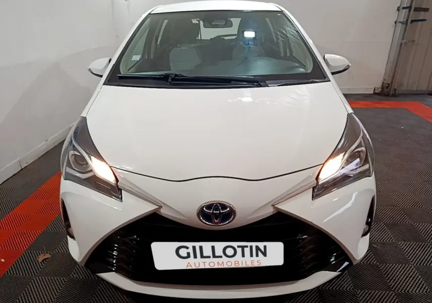 Vue avant d'une Toyota Yaris blanche 2019 avec phares allumés et calandre noire distinctive.