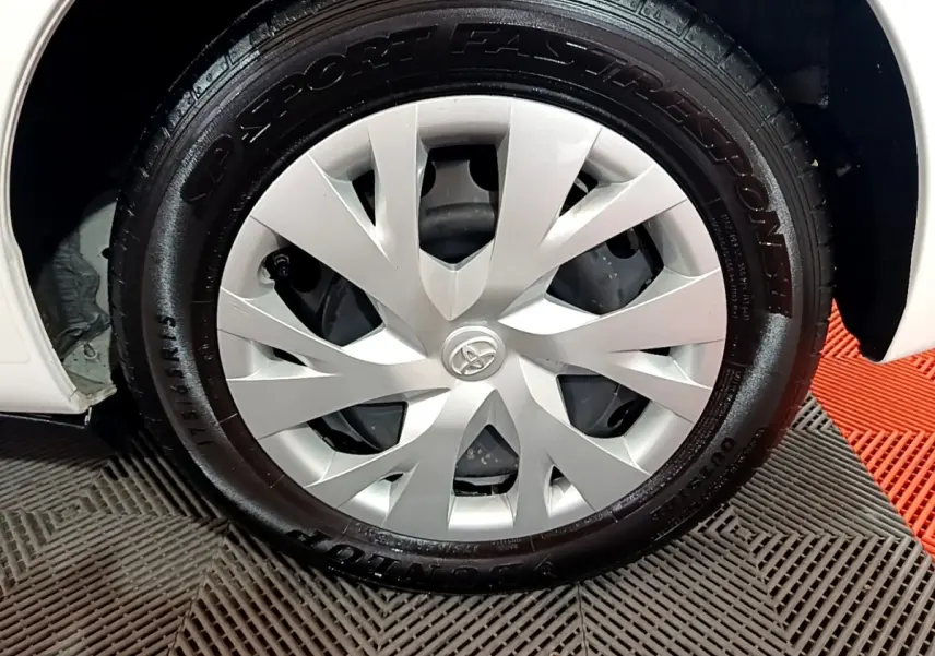 Gros plan sur la roue avant droite blanche d'une Toyota Yaris 1.5 VVT-I Hybrid France Business 2019 avec enjoliveur argenté.