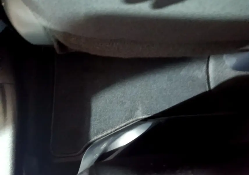 Gros plan sur le tapis de sol gris foncé sous le siège avant d'une Toyota Yaris blanche hybride 2019.