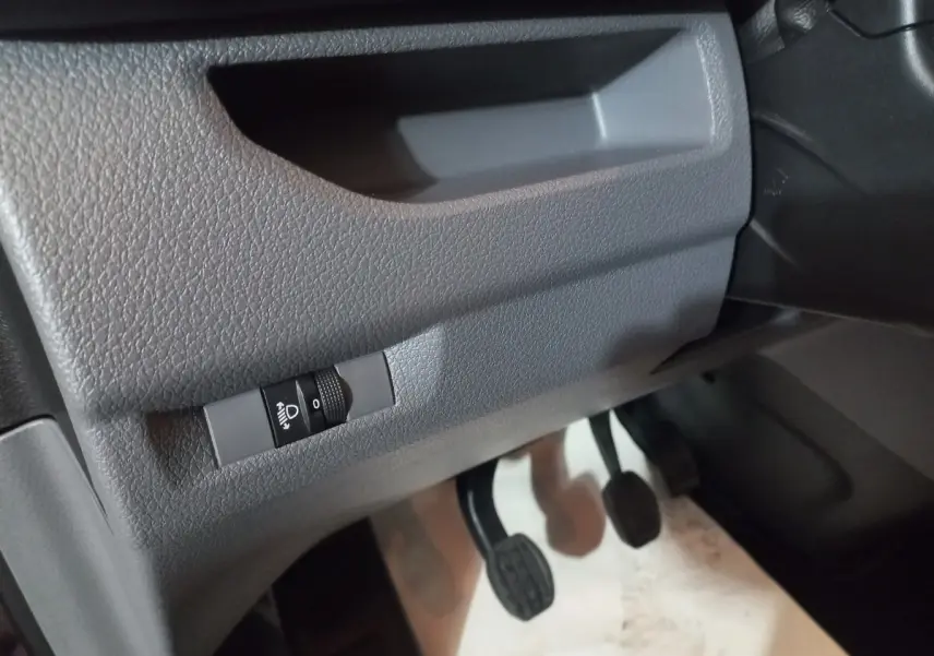 Gros plan sur la commande de réglage des phares et les pédales côté conducteur du Peugeot Traveller gris clair 2021.