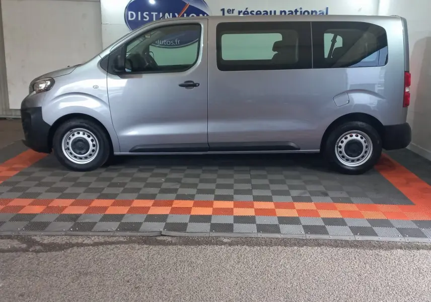 Vue latérale droite d'un Peugeot Traveller gris clair 2021 avec vitres arrière teintées et jantes acier simples.