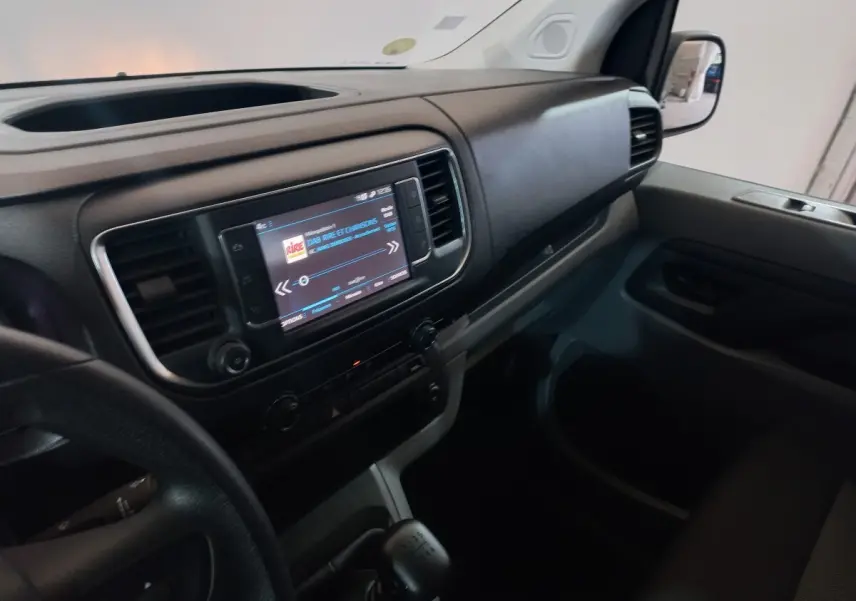 Vue intérieure côté passager du tableau de bord noir du Peugeot Traveller gris clair avec écran tactile central allumé.