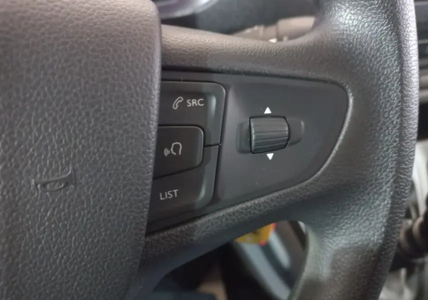 Gros plan sur les commandes noires du volant du Peugeot Traveller 1.5 BlueHDi gris clair, avec boutons SRC et LIST visibles.