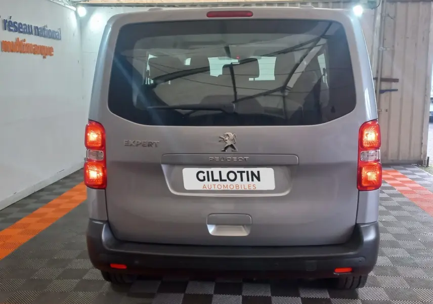 Vue arrière d’un Peugeot Traveller gris clair 2021 avec feux allumés et logo visible dans un garage.