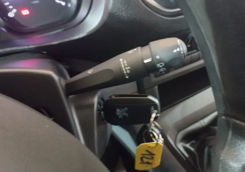 Gros plan sur la clé insérée dans le contacteur du Peugeot Traveller gris clair, avec commande d’essuie-glace visible derrière le volant.