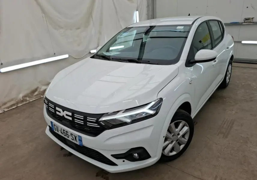 Vue 3/4 avant droit d'une Dacia Sandero blanche 2024 avec calandre noire et feux LED allumés dans un garage.