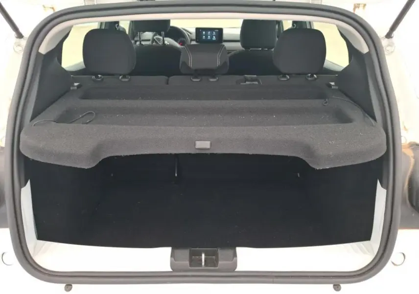 Vue arrière du coffre ouvert d'une Dacia Sandero blanche 2024, avec tablette cache-bagages et sièges arrière visibles.