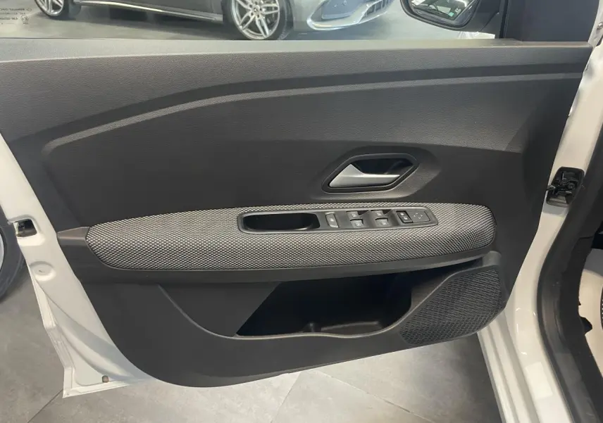Vue rapprochée de la porte avant gauche blanche d’une Dacia Sandero 2024 avec commandes de vitres et poignée grise.