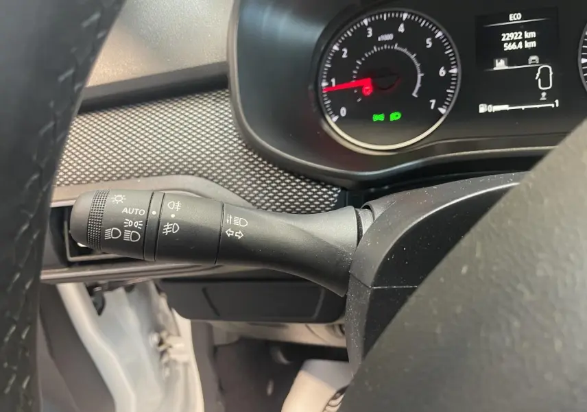 Gros plan sur le commodo gauche du tableau de bord d’une Dacia Sandero blanche, avec compteurs et affichage numérique.