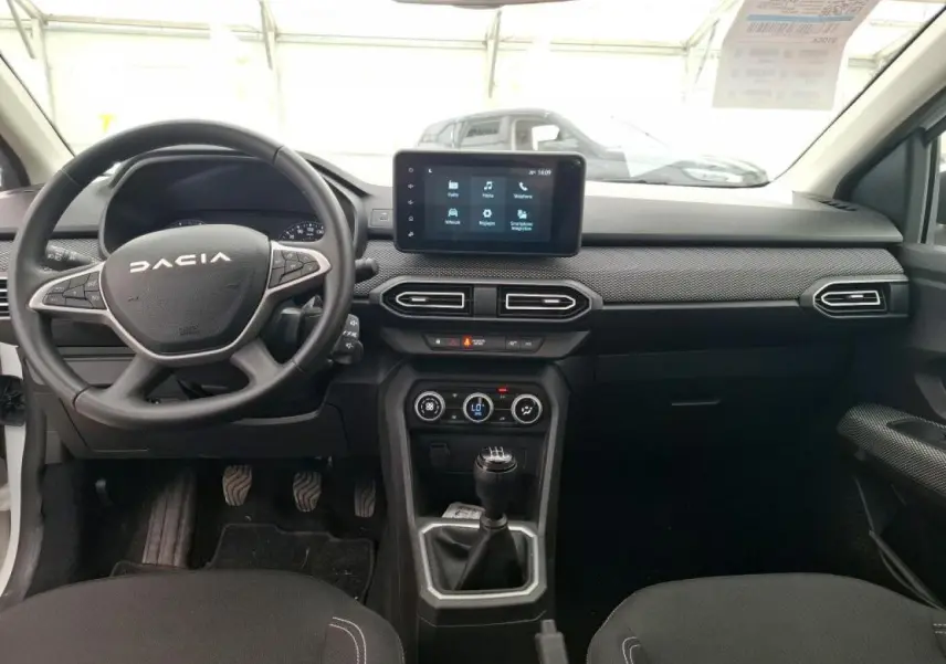 Vue intérieure avant de la Dacia Sandero blanche 2024, tableau de bord avec écran tactile et volant multifonction.