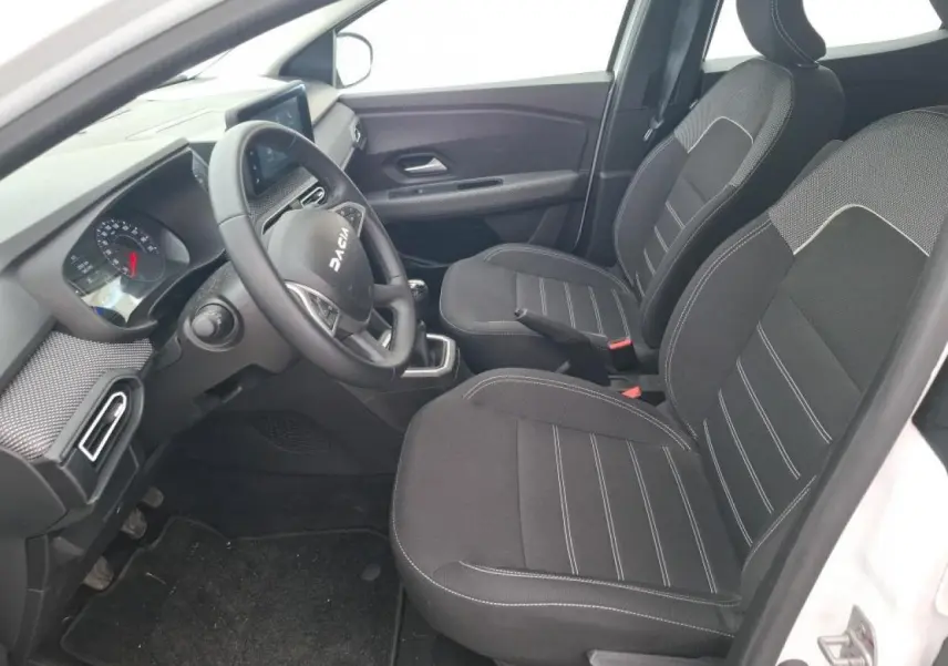 Vue intérieure côté conducteur de la Dacia Sandero blanche 2024, avec sellerie tissu noire et volant multifonction.