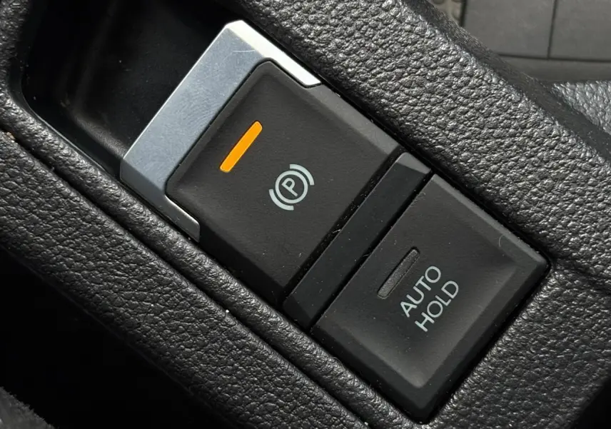 Gros plan sur le bouton de frein de stationnement électromécanique et fonction Auto Hold dans l’habitacle noir du Volkswagen T-Roc.