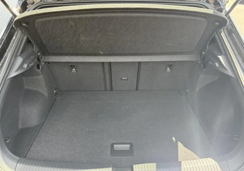 Coffre ouvert du Volkswagen T-Roc noir intense 2025, vue arrière montrant l'espace de chargement vide et le cache-bagages relevé.