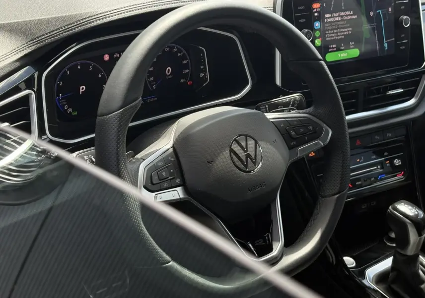 Vue rapprochée du volant cuir noir avec logo Volkswagen et tableau de bord digital du Volkswagen T-Roc 1.5 TSI R-Line 2025.