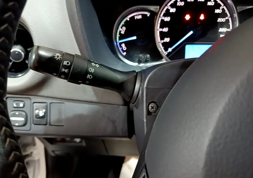 Gros plan sur le tableau de bord et commodo gauche de la Toyota Yaris hybride blanche de 2019, avec compte-tours et vitesse visibles.