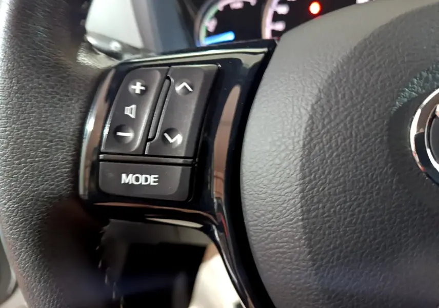 Gros plan sur les commandes gauche du volant cuir noir de la Toyota Yaris hybride blanche, avec tableau de bord en arrière-plan.