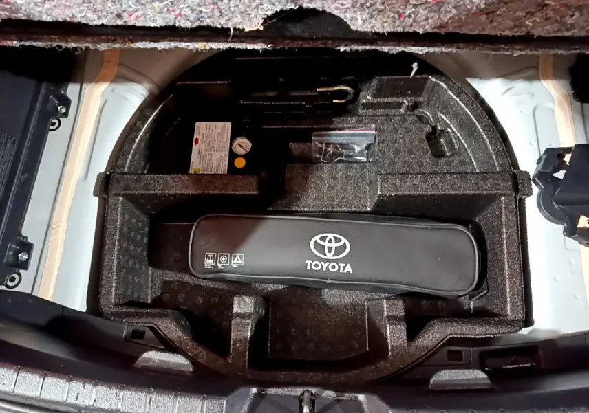 Vue plongeante sur le coffre ouvert d'une Toyota Yaris blanche, montrant le rangement sous tablette avec kit de secours Toyota.