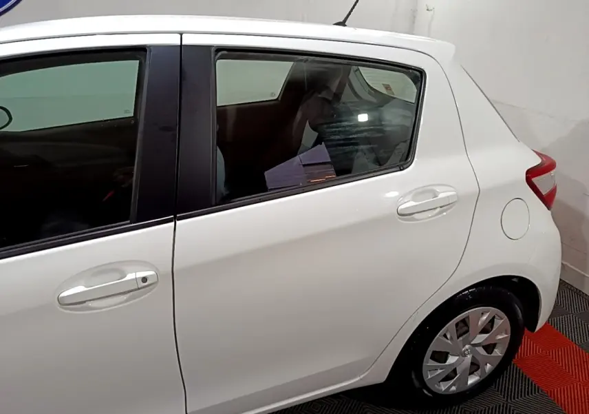 Vue latérale côté droit d'une Toyota Yaris blanche 2019, mettant en valeur la porte arrière et la roue arrière.