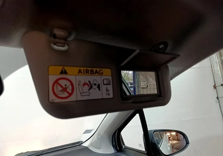 Détail du pare-soleil avec miroir et avertissement airbag, vue intérieure côté conducteur d'une Toyota Yaris blanche.