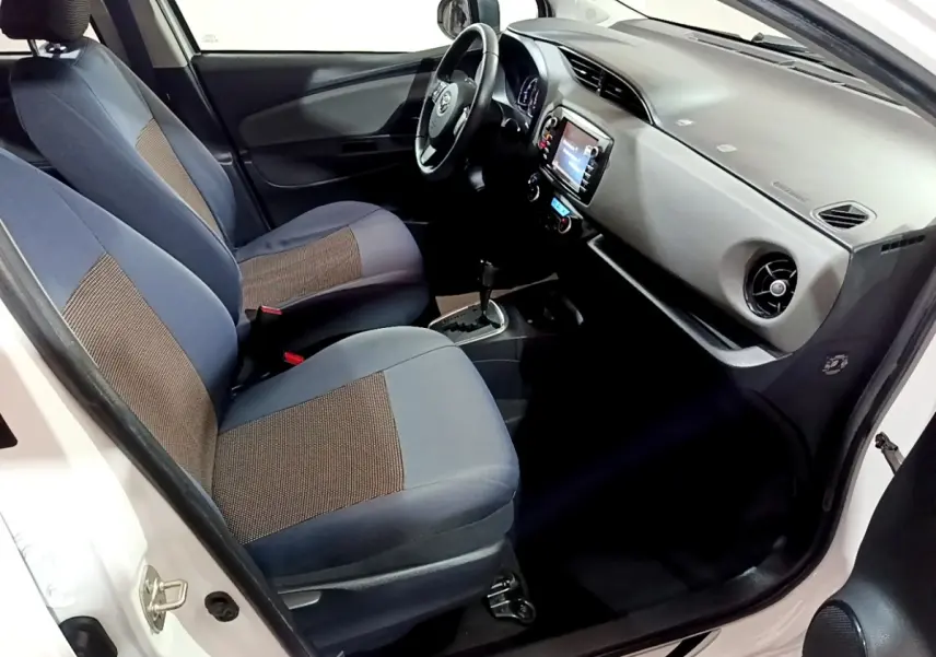 Vue intérieure côté conducteur de la Toyota Yaris blanche 2019, sièges tissu bicolore et tableau de bord avec écran tactile.