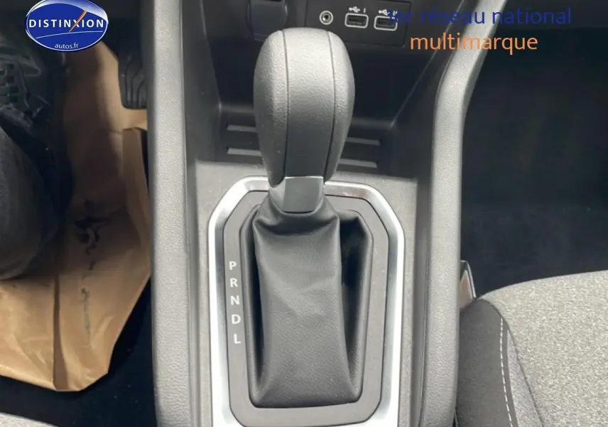 Gros plan sur le levier de vitesse automatique noir de la Renault Clio V essence, intérieur tissu gris visible à droite.