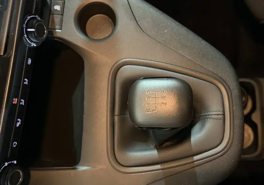 Gros plan sur le levier de vitesses manuel noir du Peugeot Rifter blanc, avec console centrale et commandes climatisation visibles.