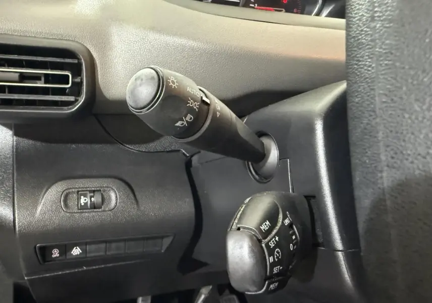 Gros plan sur la commande des phares et régulateur de vitesse à gauche du volant dans l’habitacle noir du Peugeot Rifter blanc 2019.