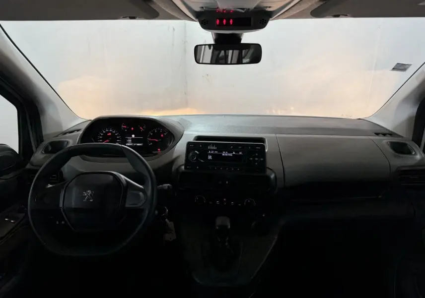 Vue intérieure frontale du tableau de bord et volant noir du Peugeot Rifter blanc, avec affichage digital et commandes centrales visibles.