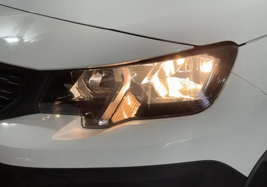 Gros plan sur le phare avant droit allumé d’un Peugeot Rifter blanc, mettant en valeur les détails du bloc optique.