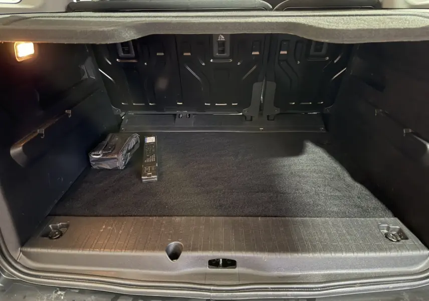 Coffre ouvert vu de l'arrière d'un Peugeot Rifter blanc, montrant un espace de chargement propre avec accessoires rangés.