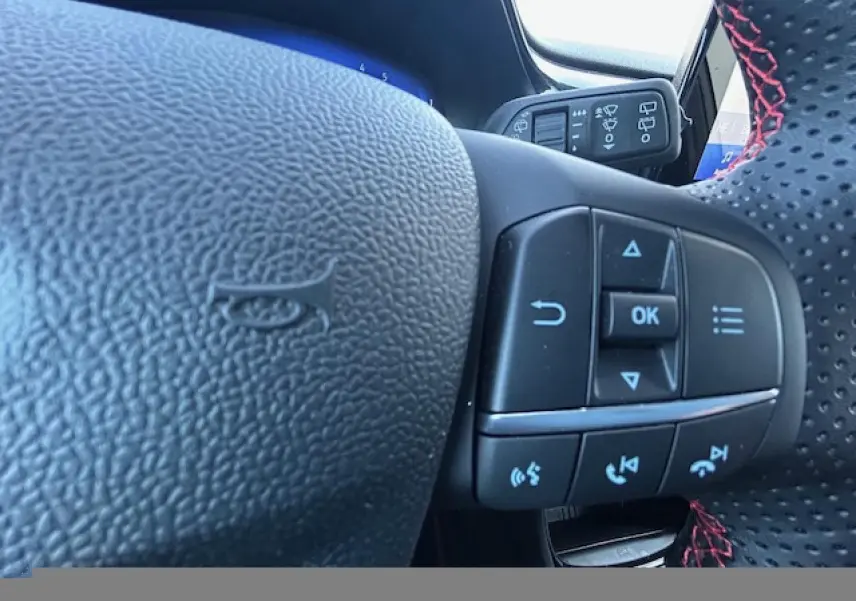 Gros plan sur le volant perforé avec surpiqûres rouges et commandes multifonctions du Ford Puma gris Solar 2023.