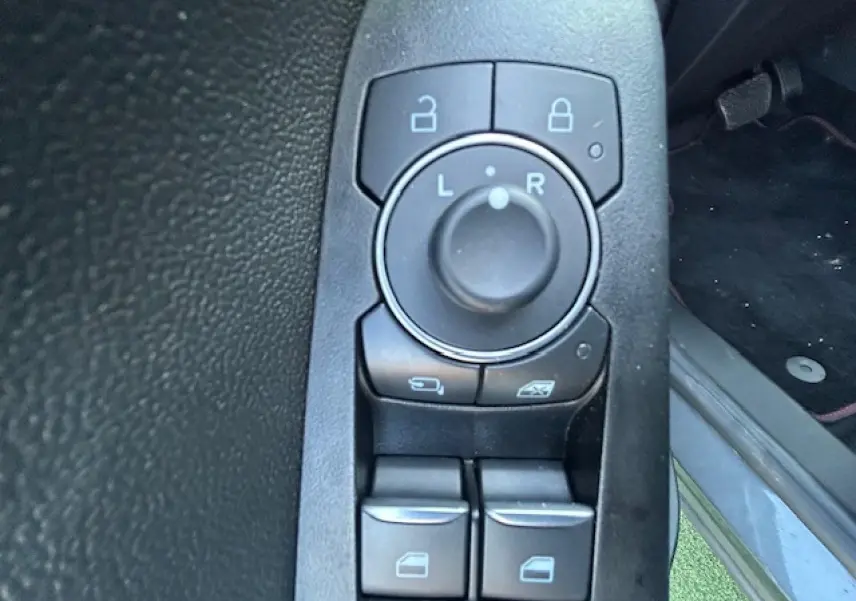 Gros plan sur les commandes de réglage des rétroviseurs et des vitres côté conducteur du Ford Puma gris Solar 2023.