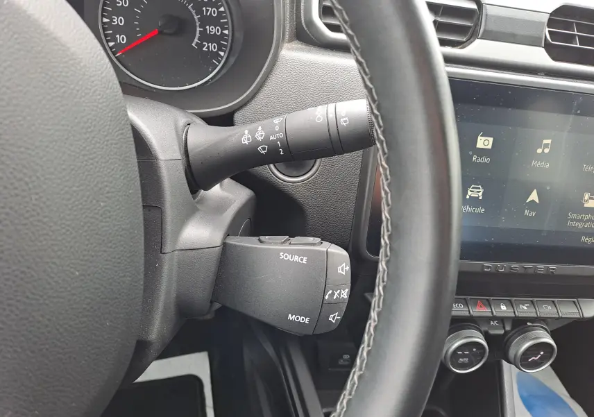 Vue rapprochée du volant et de la commande multimédia du Dacia Duster 2024 gris urbain, avec écran tactile et tableau de bord.
