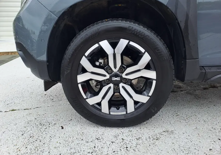 Gros plan sur la roue avant gauche du Dacia Duster gris urbain 2024 avec jante alliage bicolore et pneu Bridgestone.